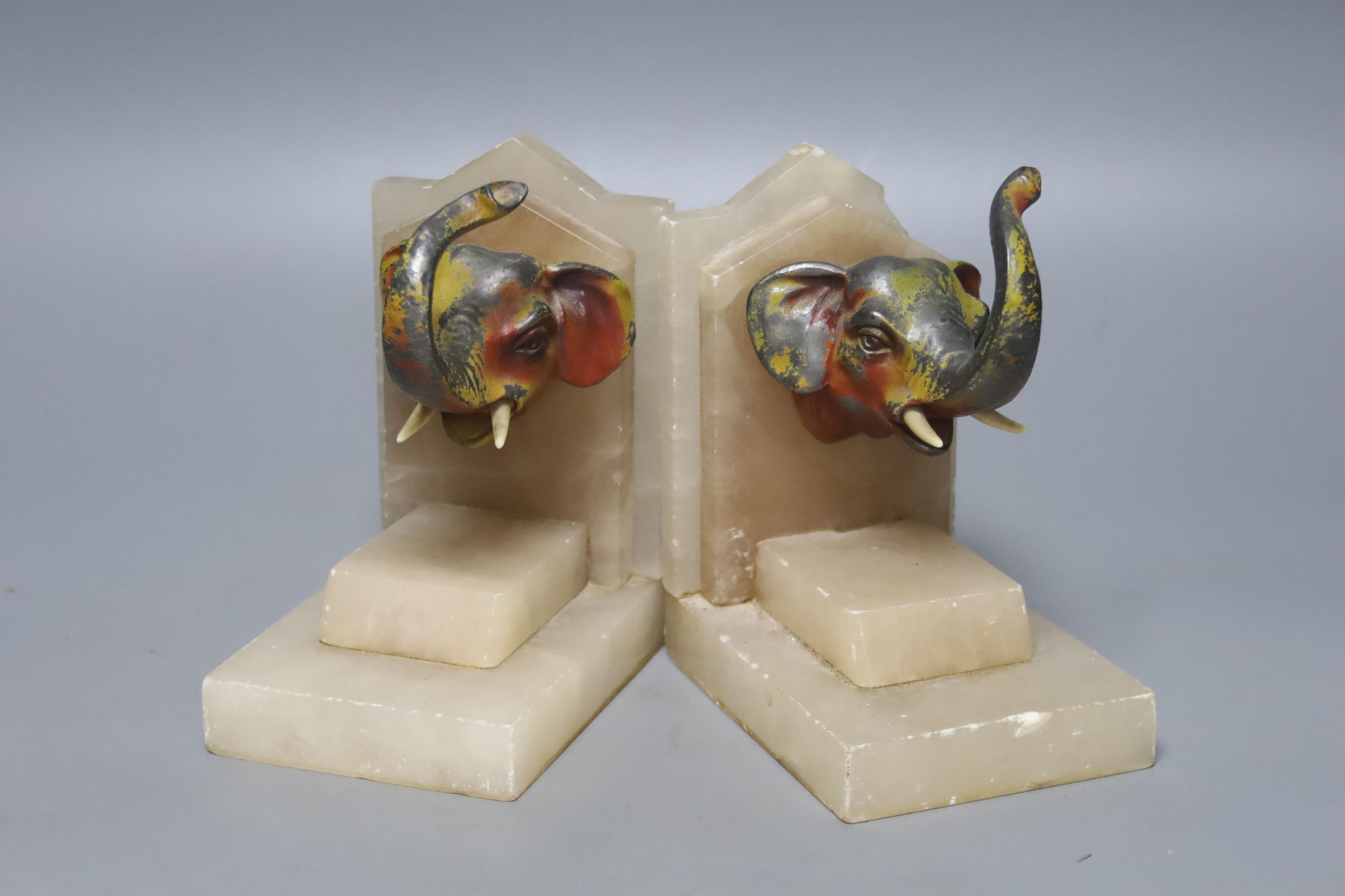 A pair of 1930's alabaster book ends, each applied with a painted metal elephant head, 14cm